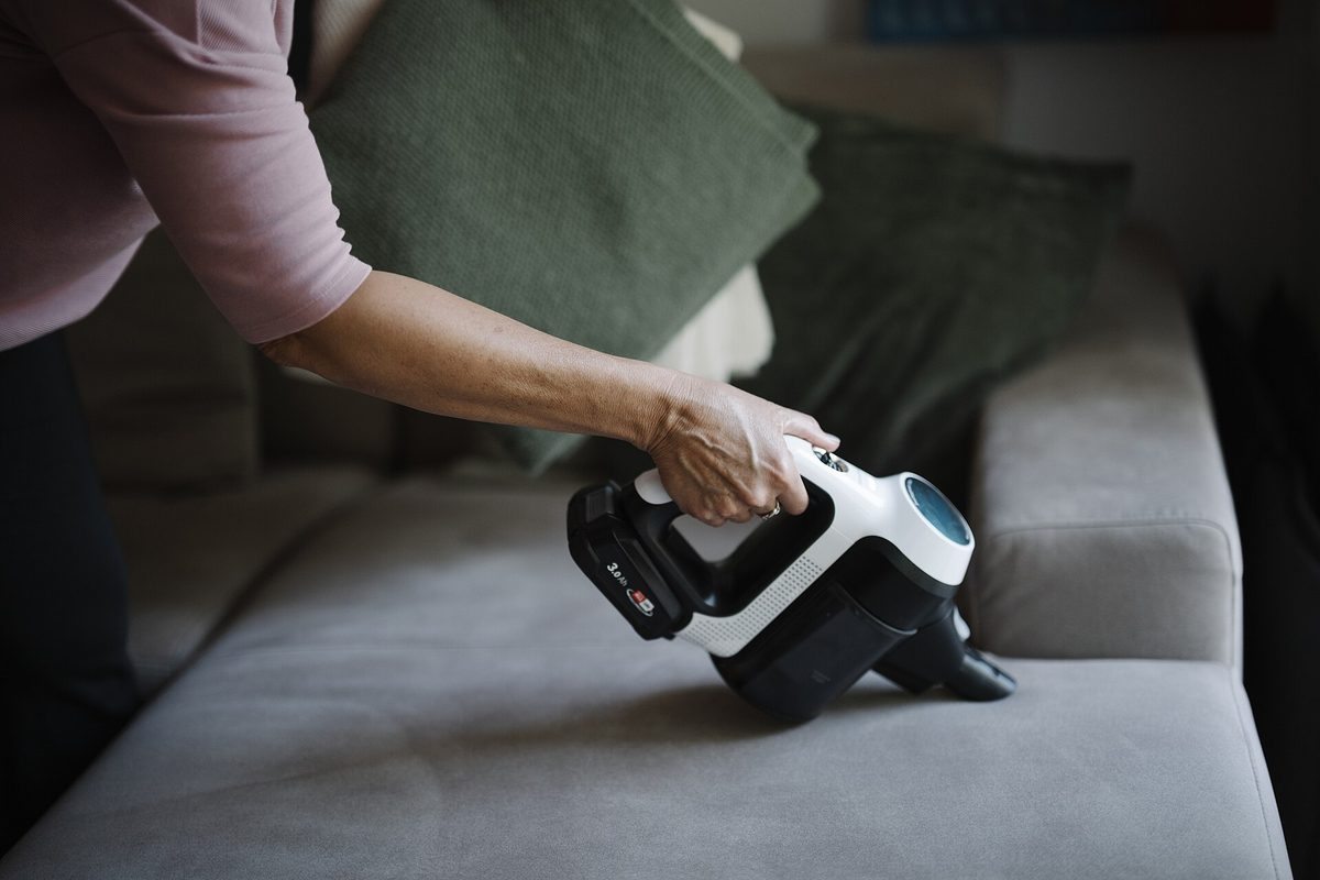 Người dùng máy hút bụi cầm tay dọn sofa trong phòng khách